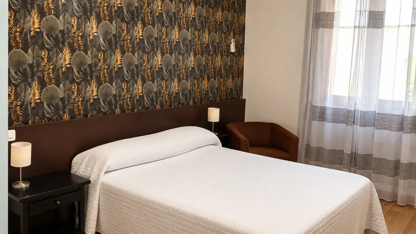Dormitorio con una cama blanca impecablemente hecha, una pared decorativa con estampado