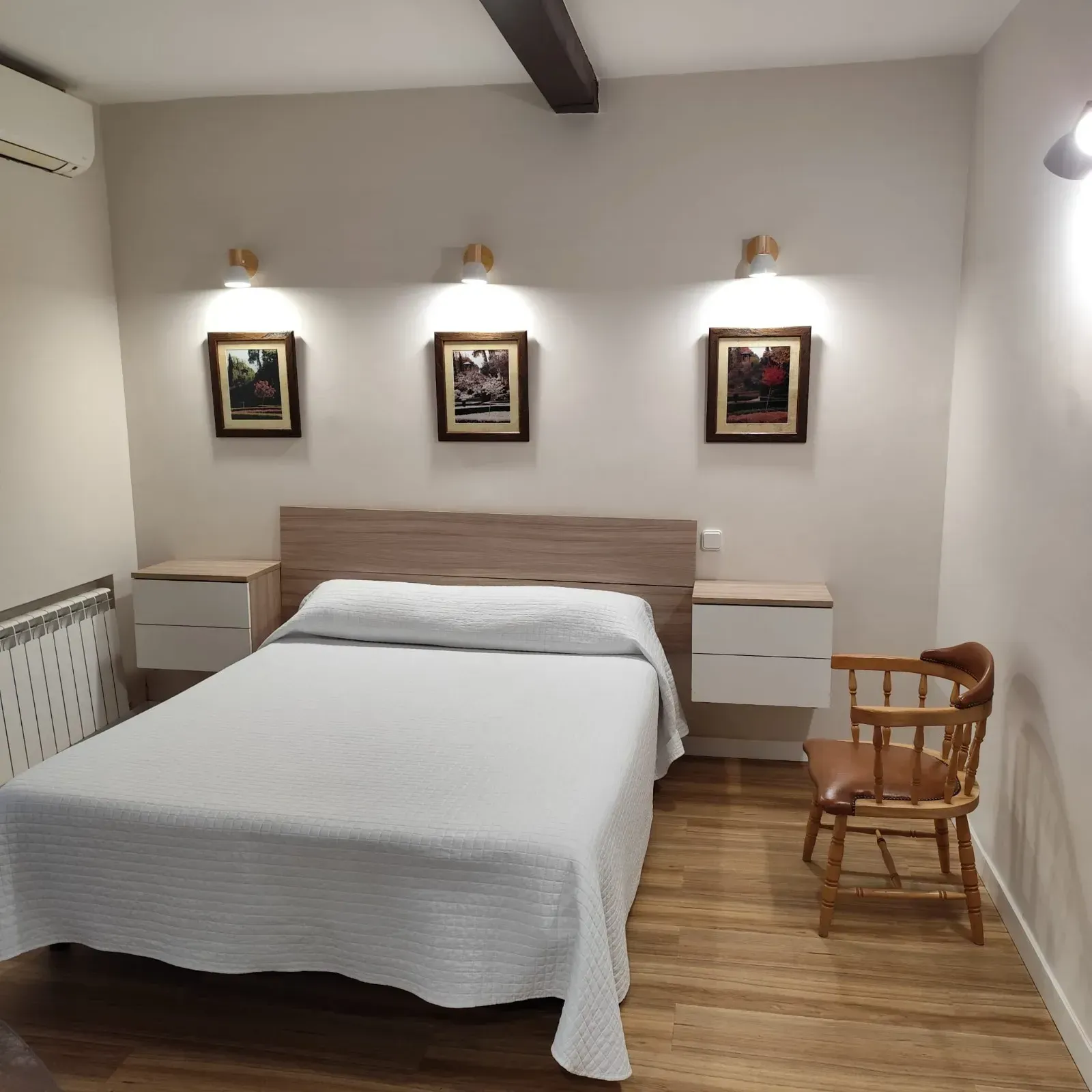Acogedora habitación con cama doble, ropa de cama blanca, silla de madera, mesitas de noche