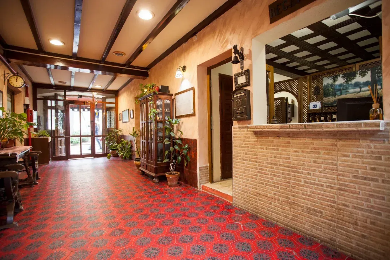 Vestíbulo vacío de un restaurante con alfombra roja estampada, mostrador de servicio de ladrillo y plantas en macetas.