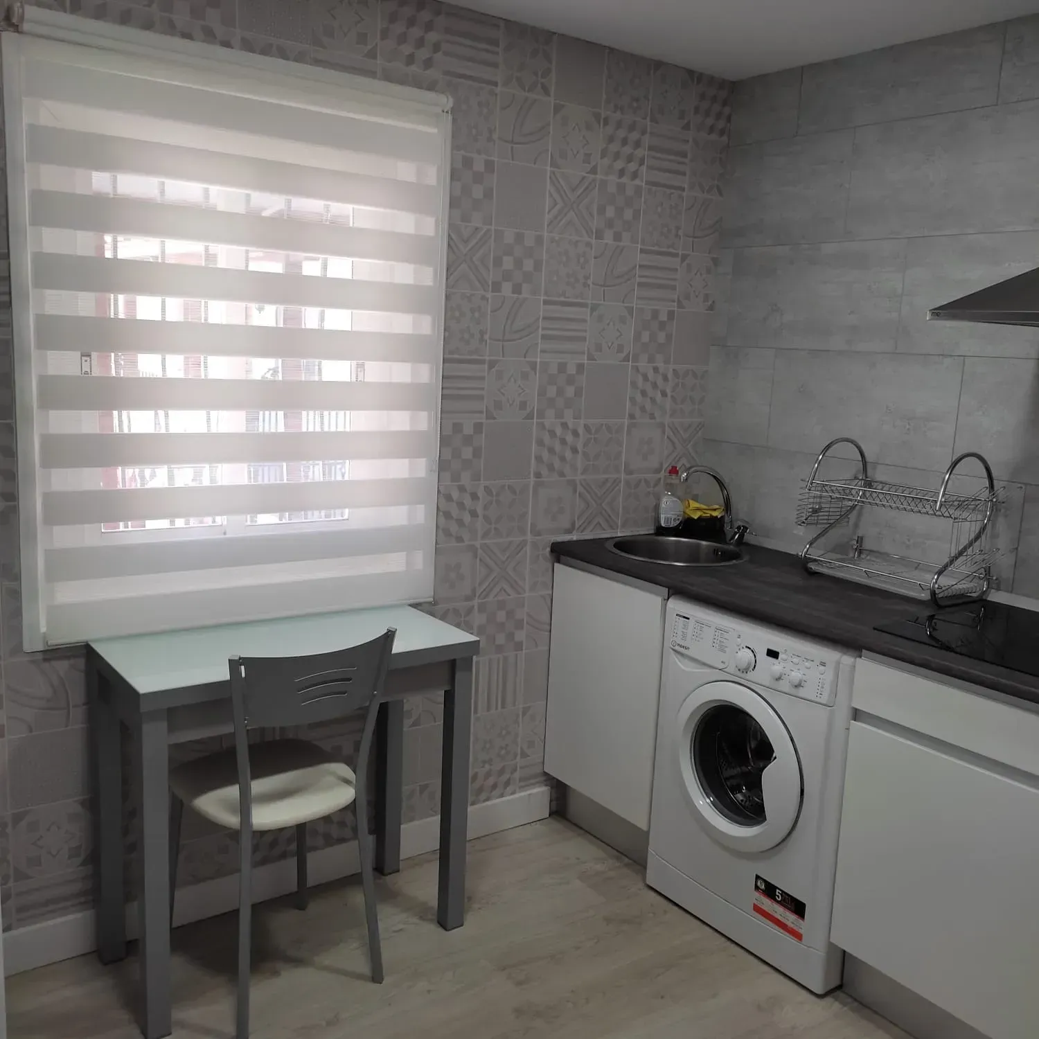 Cuarto de lavandería compacto con un pequeño escritorio junto a la ventana, lavadora, fregadero y armarios blancos.