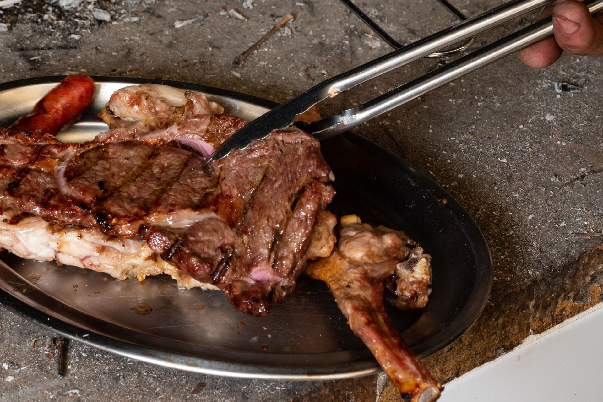 Una persona está cortando un trozo de carne en un plato con pinzas.