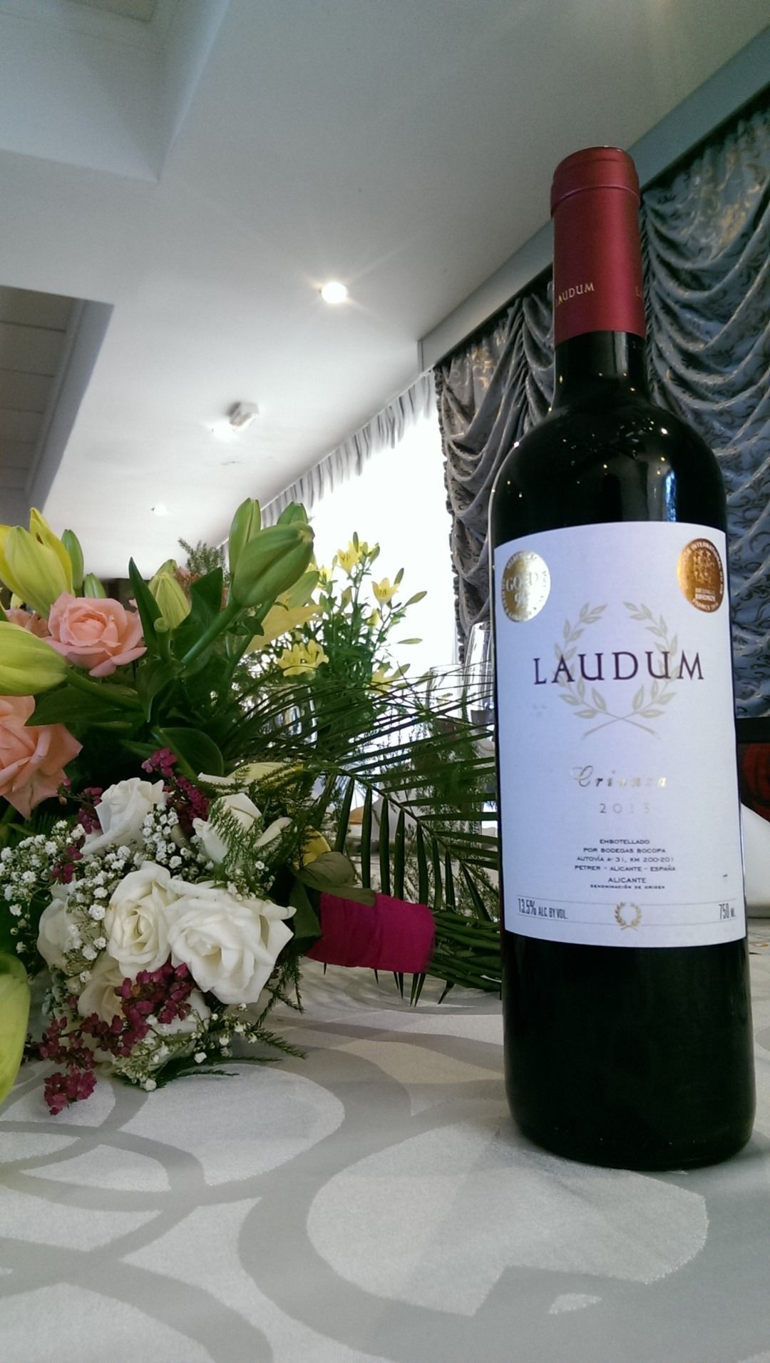 Una botella de vino laudun está sobre una mesa con flores al fondo.