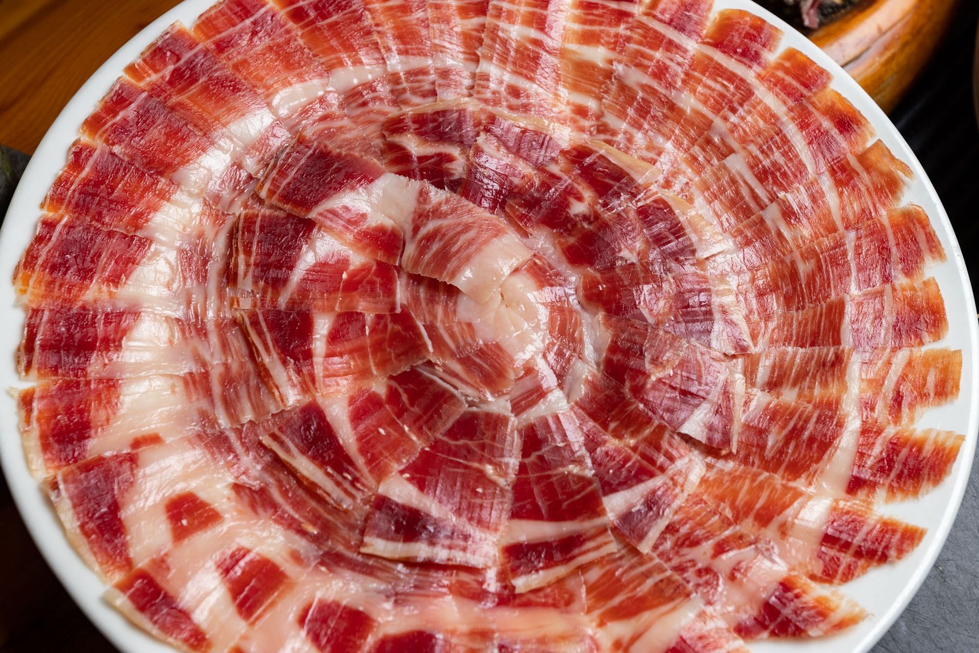 Un plato blanco cubierto con rodajas de jamón sobre una mesa.