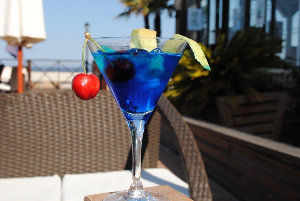 Un martini azul con una cereza encima.