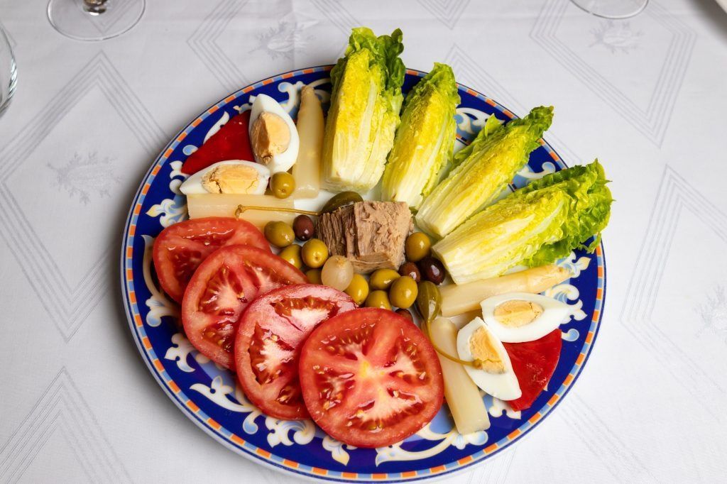 Un plato de comida con lechuga, tomates, huevos y aceitunas.