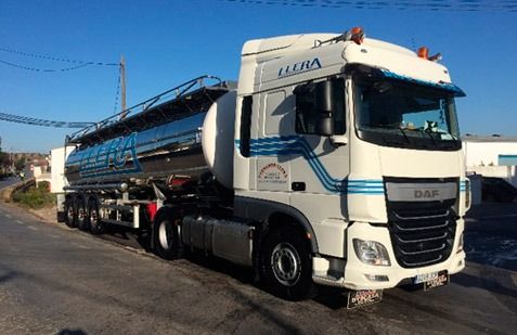 Un camión semirremolque blanco arrastrando un largo remolque cisterna azul por una carretera bajo un cielo despejado.