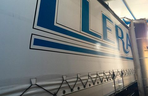 Gran remolque de camión azul y blanco con letras llamativas, visto de lado a la luz del día.