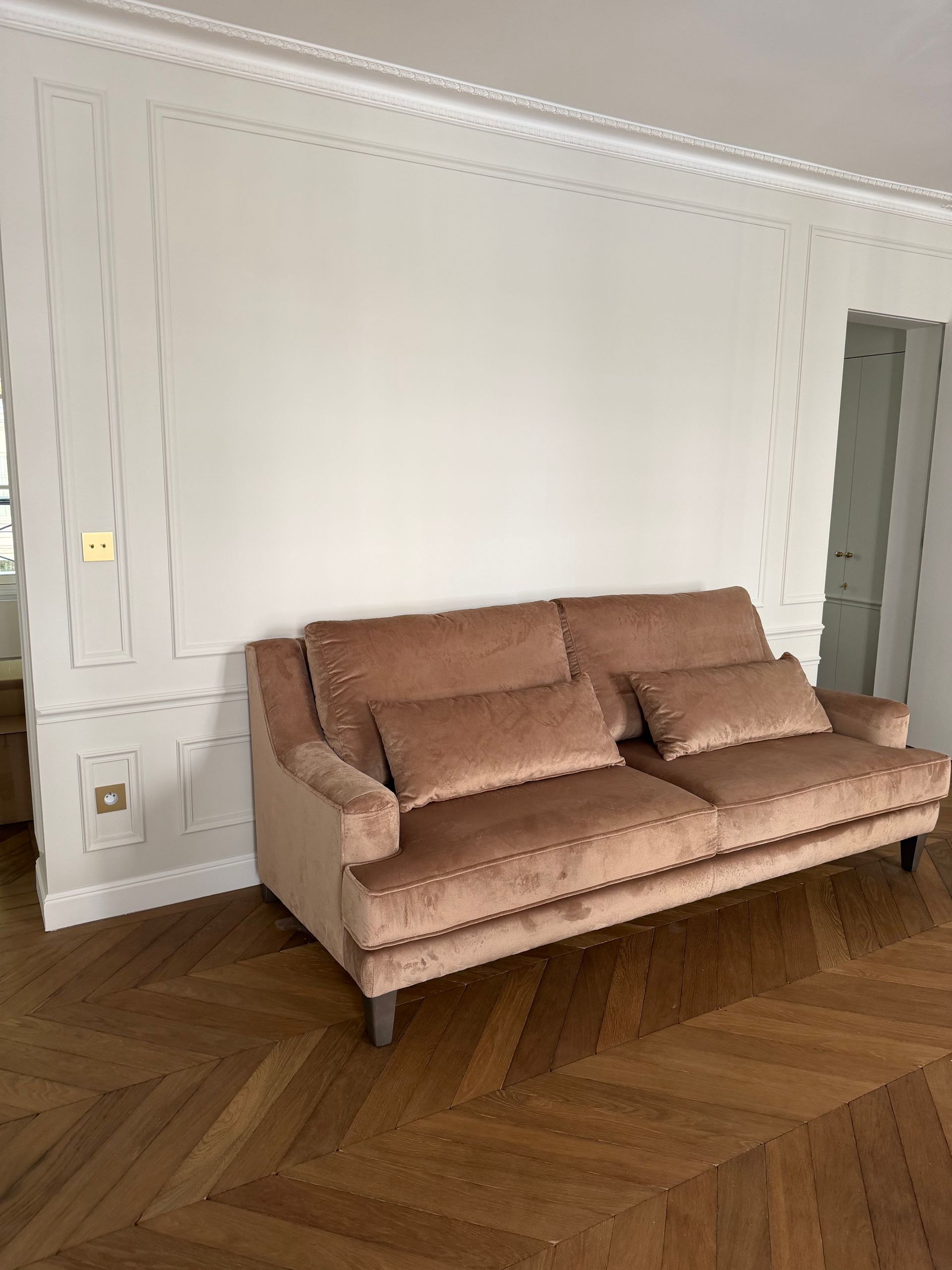 Canapé rose contre un mur blanc dans une pièce lumineuse avec parquet à chevrons