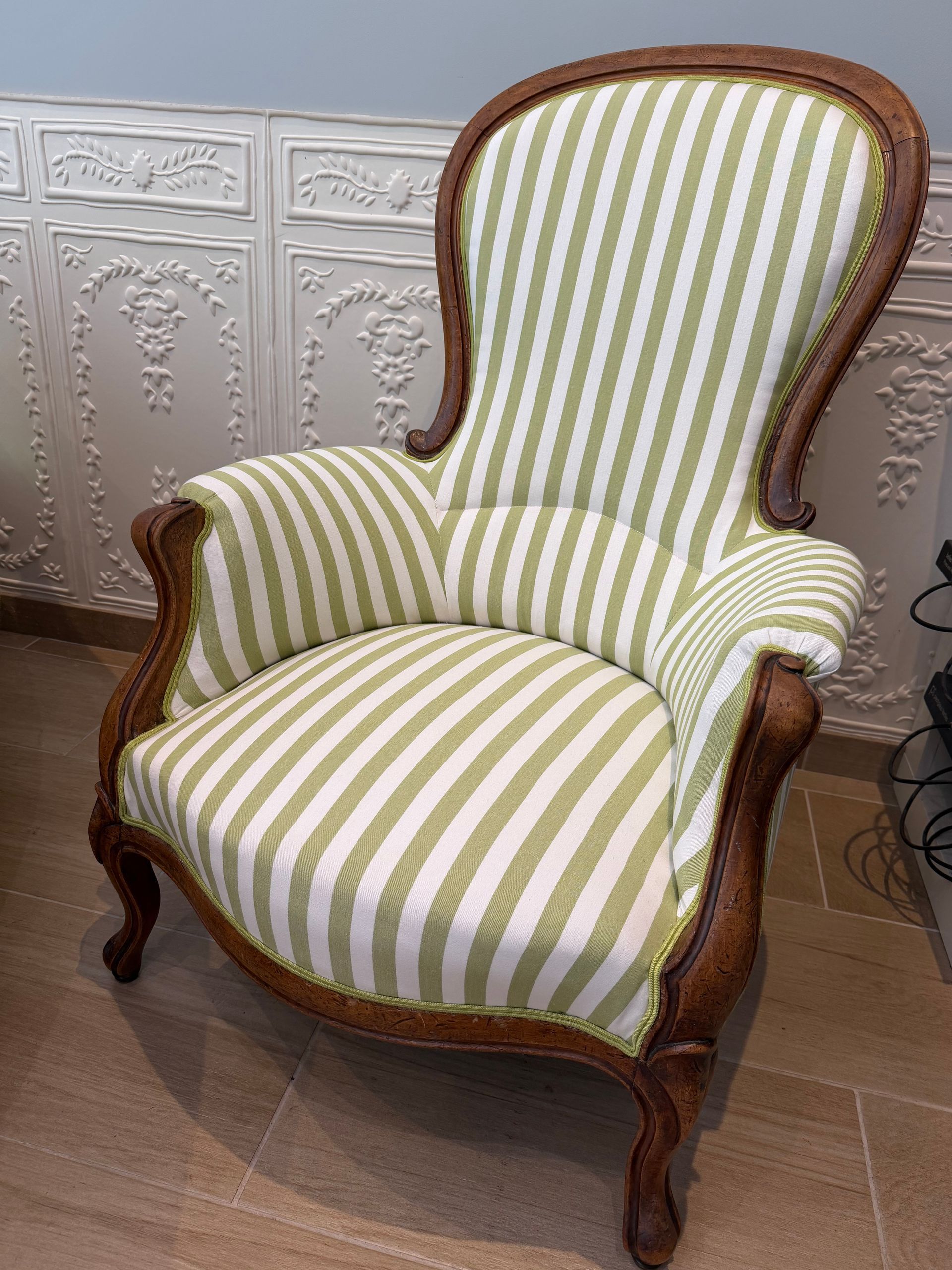 Fauteuil capitonné à rayures vertes et crème avec pieds en bois sculpté dans une pièce.