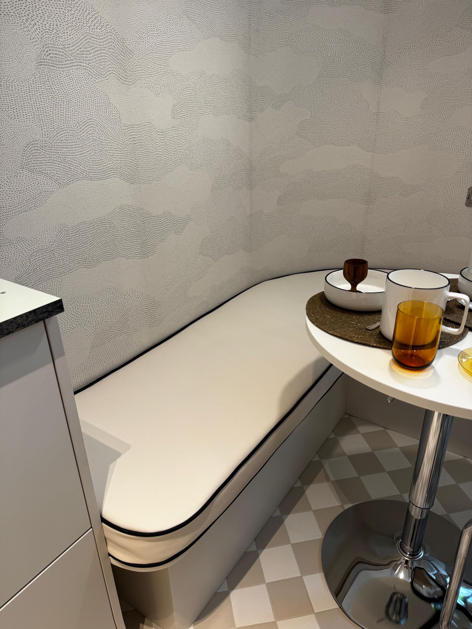Petit coin café avec une banquette blanche et une table ronde où sont disposés boissons et desserts.