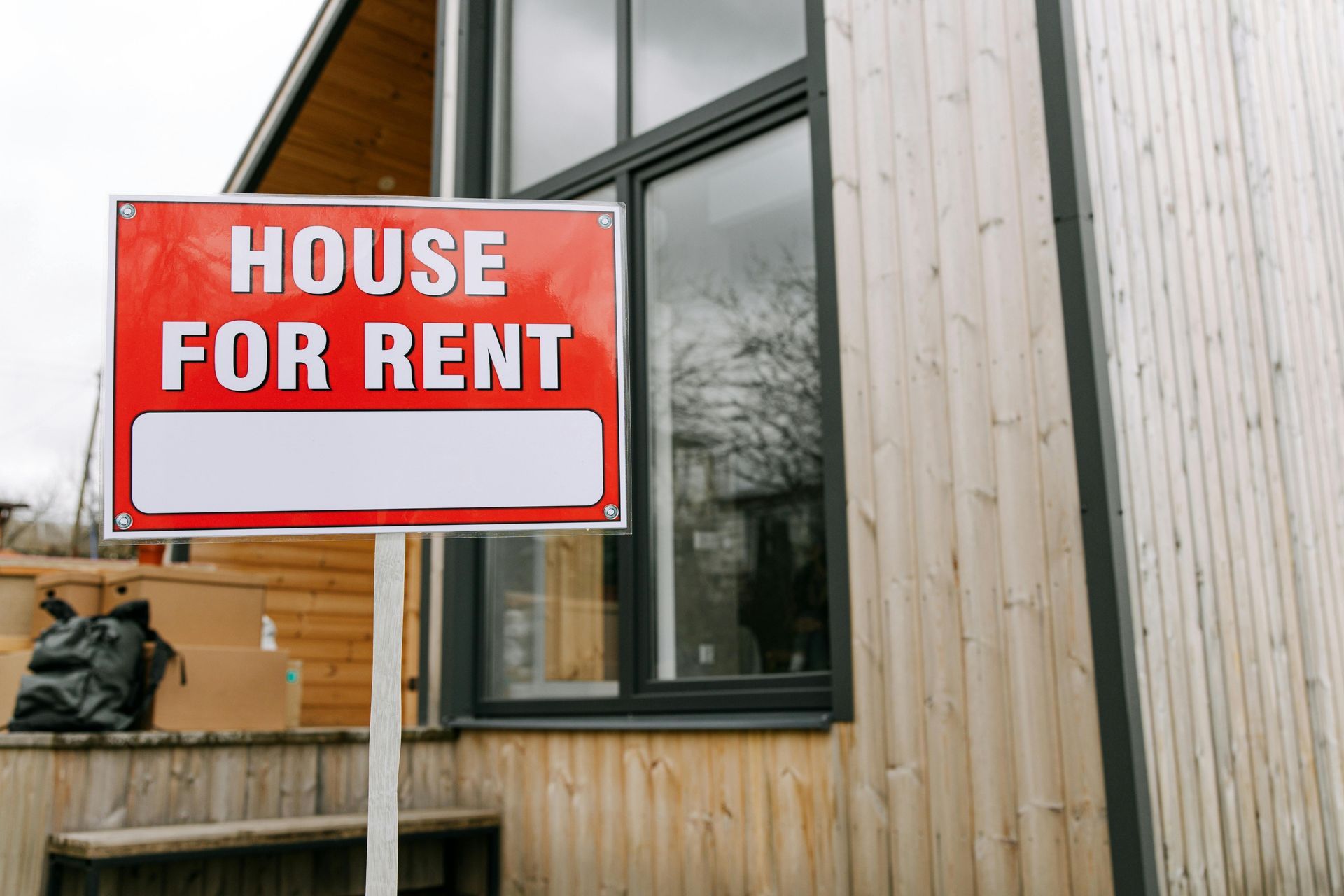 A house for rent sign is in front of a wooden house, property investor