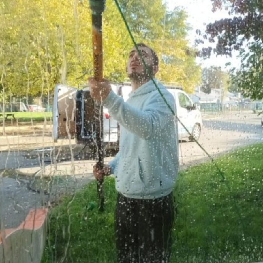 Un homme lave une vitre avec un outil à long manche, debout à l'extérieur, avec une camionnette blanche en arrière-plan.
