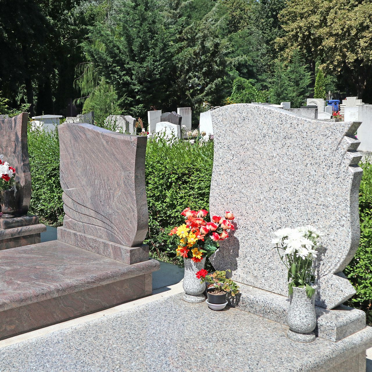 Deux pierres tombales en granit richement ornées, agrémentées de vases à fleurs, dans un cimetière.