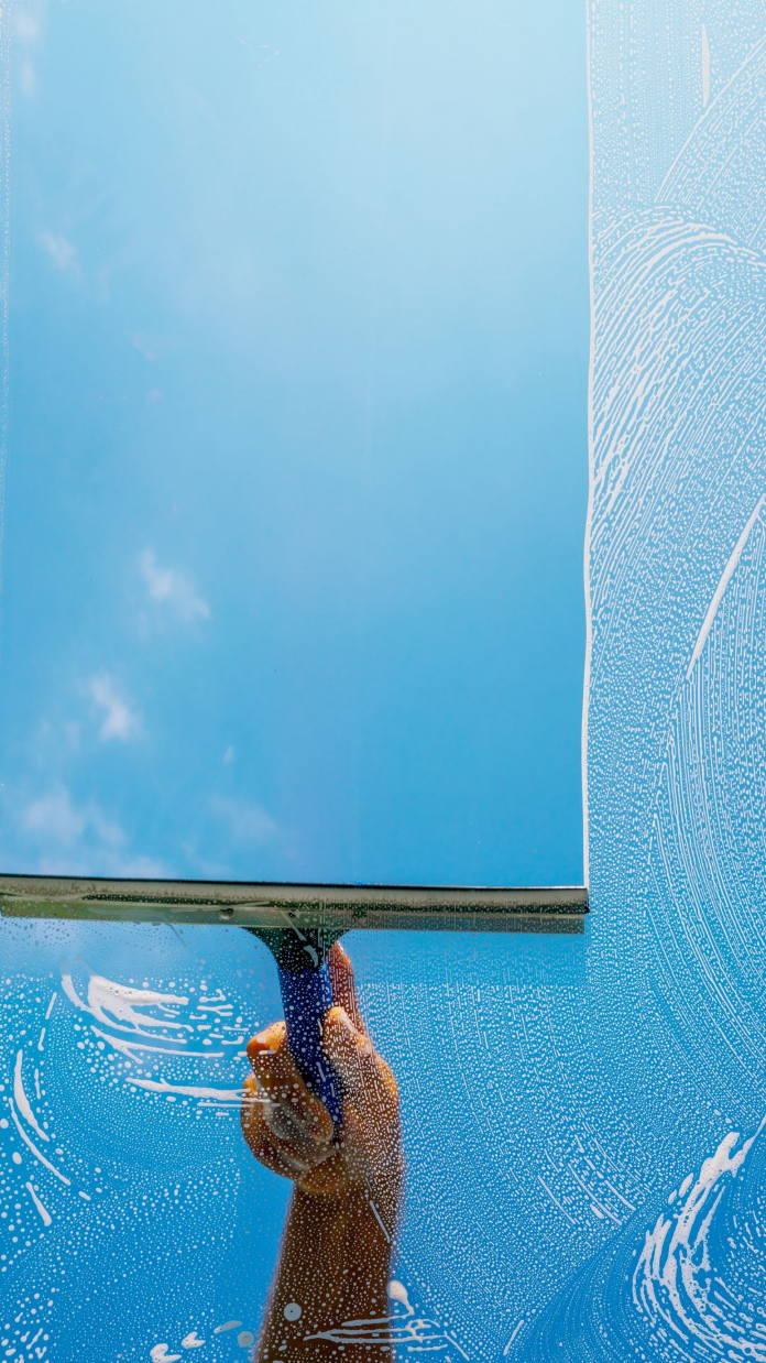 Main tenant une raclette nettoyant une vitre, ciel dégagé visible à travers la zone nettoyée.