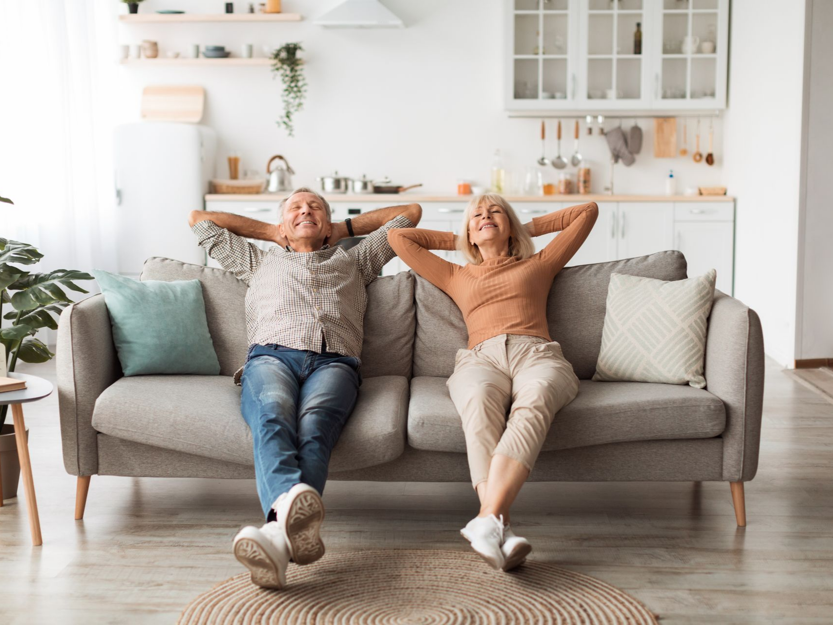 Un couple se détend sur un canapé dans un salon, les mains derrière la tête, souriant.