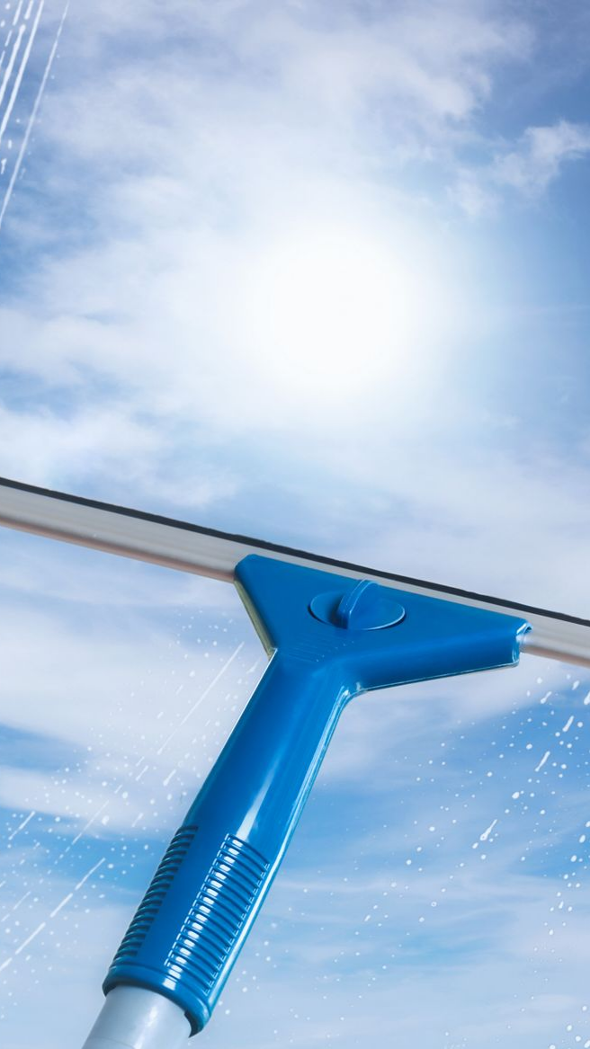 Une raclette à manche bleu nettoie une vitre, avec un ciel bleu vif et des nuages ​​en arrière-plan.