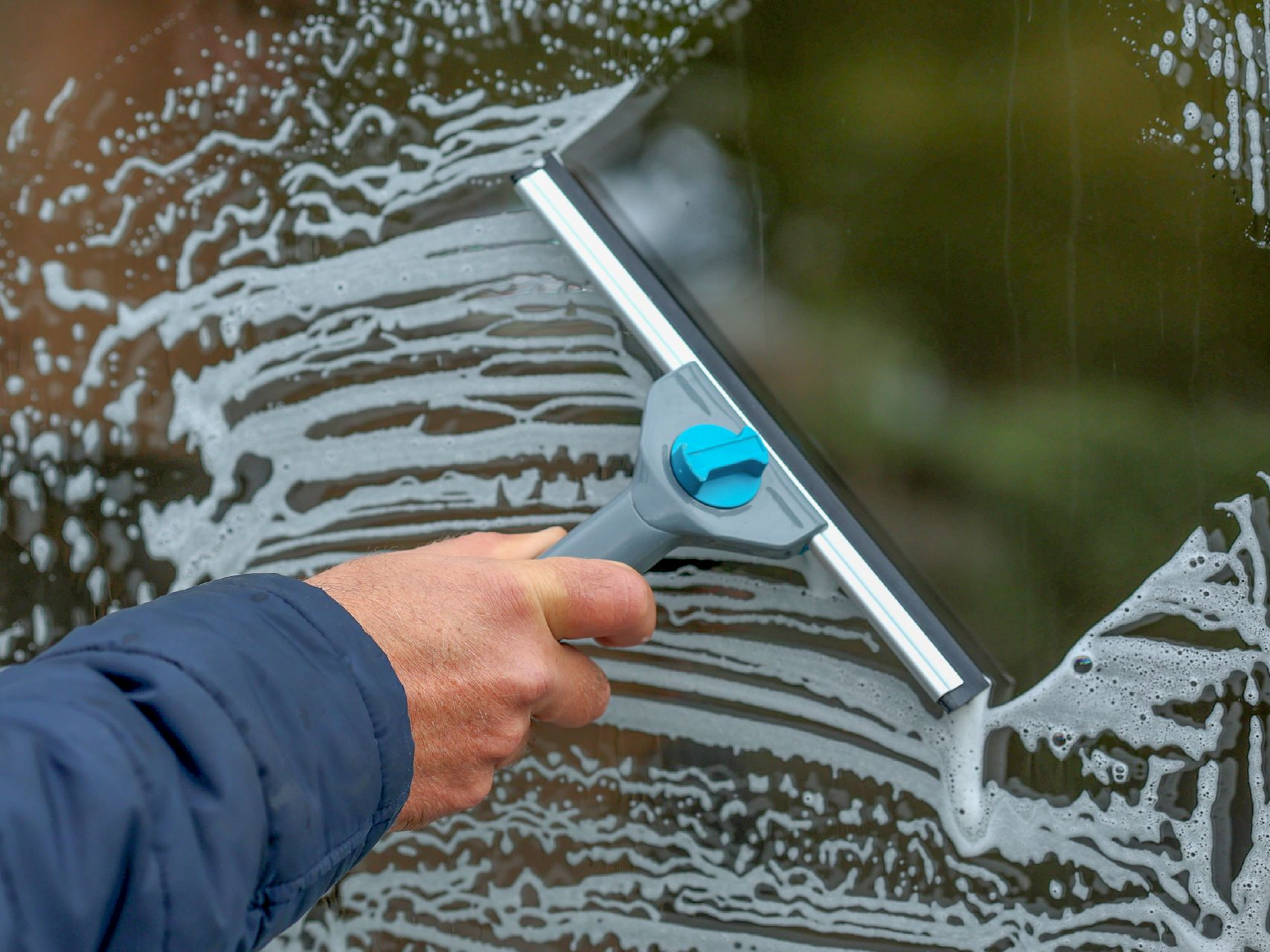 Main tenant une raclette nettoyant une vitre savonneuse.