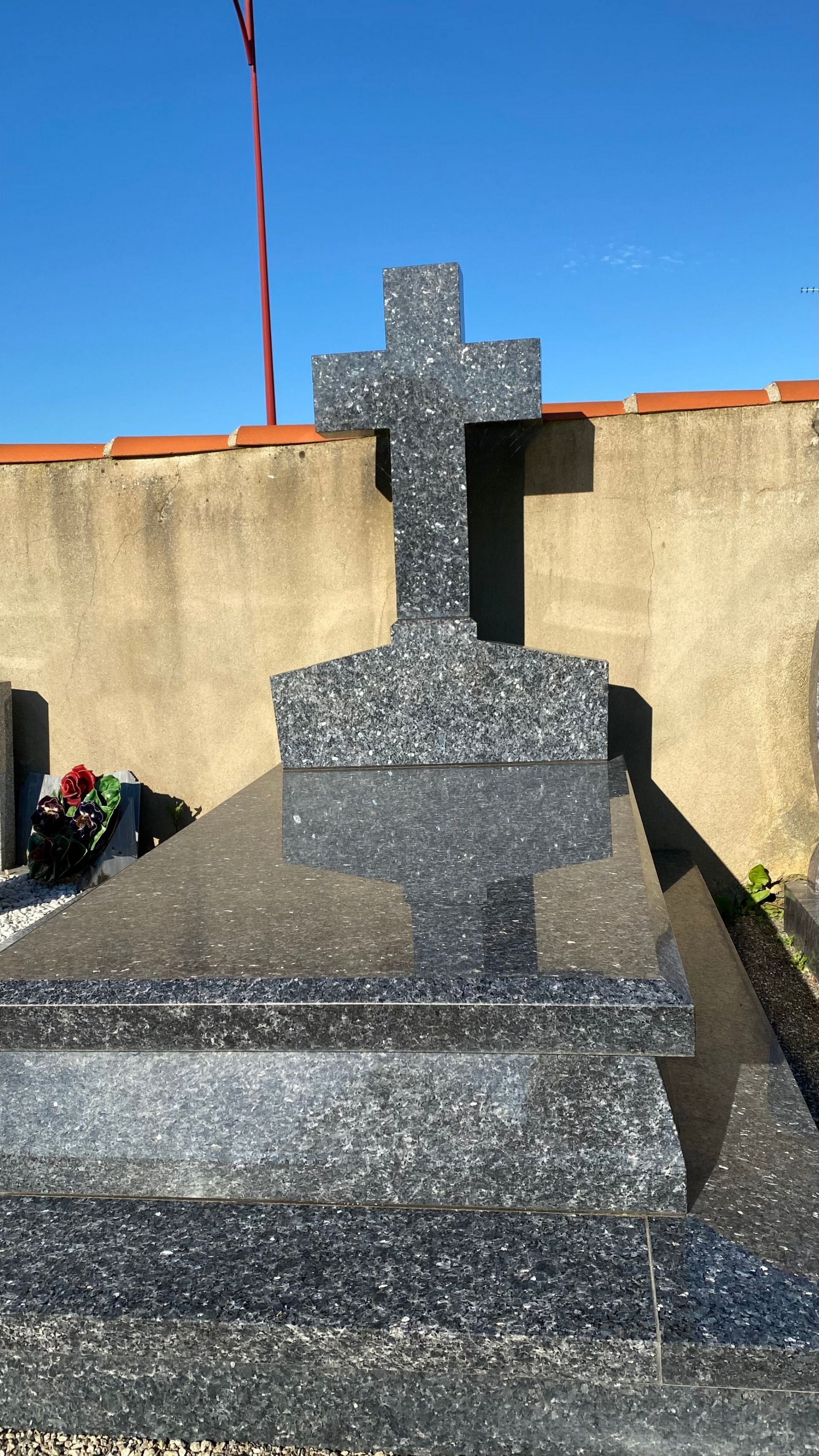 Tombe ornée d'une croix et d'une pierre tombale en marbre devant un mur, le ciel est bleu.