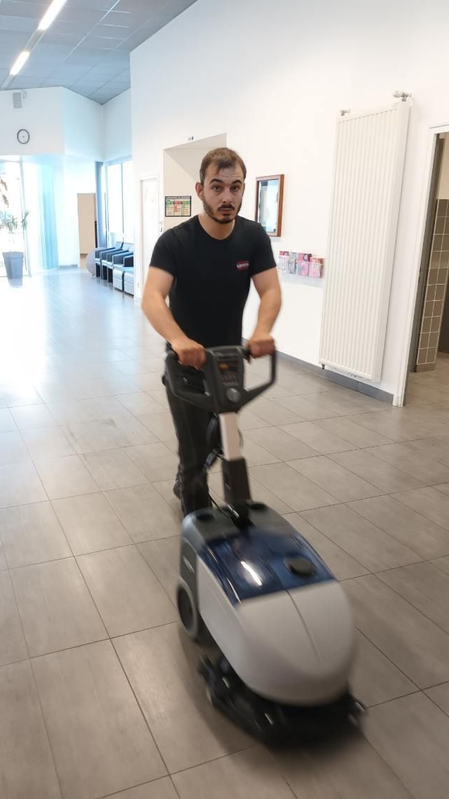 Un homme utilise une machine de nettoyage de sol dans un couloir.