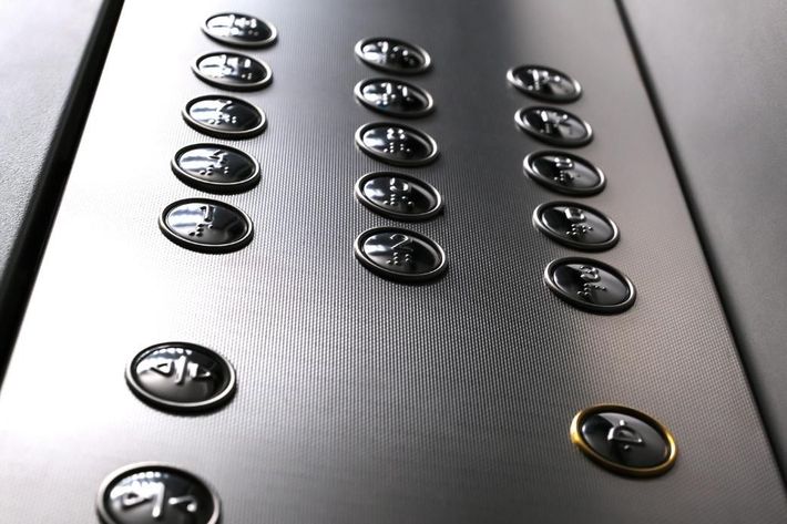 Primer plano de botones metálicos de ascensor dispuestos en filas sobre un panel de acero cepillado.