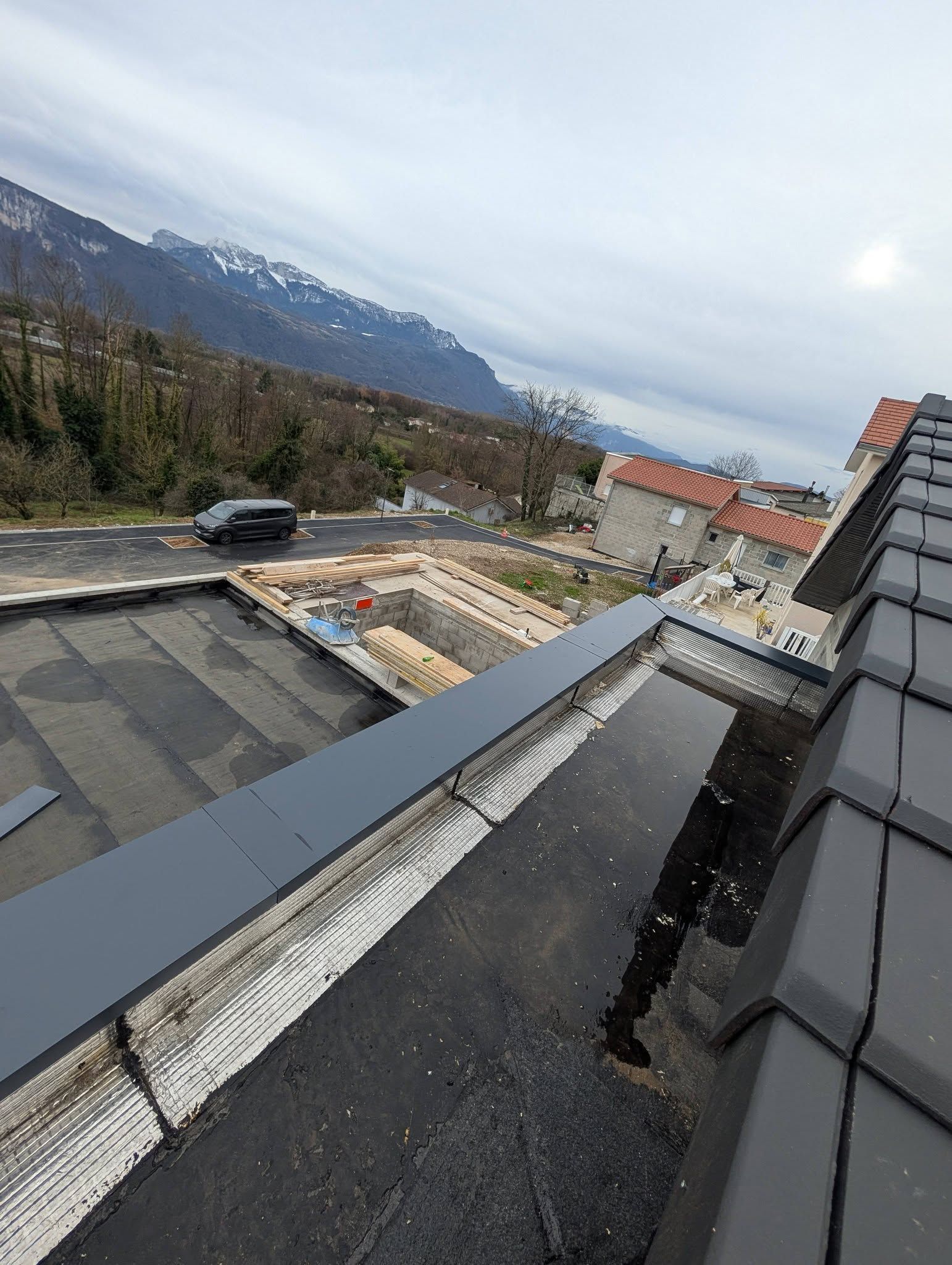 Vue en plongée d'un toit plat en construction, montrant des matériaux d'étanchéité sombres et des solins métalliques.