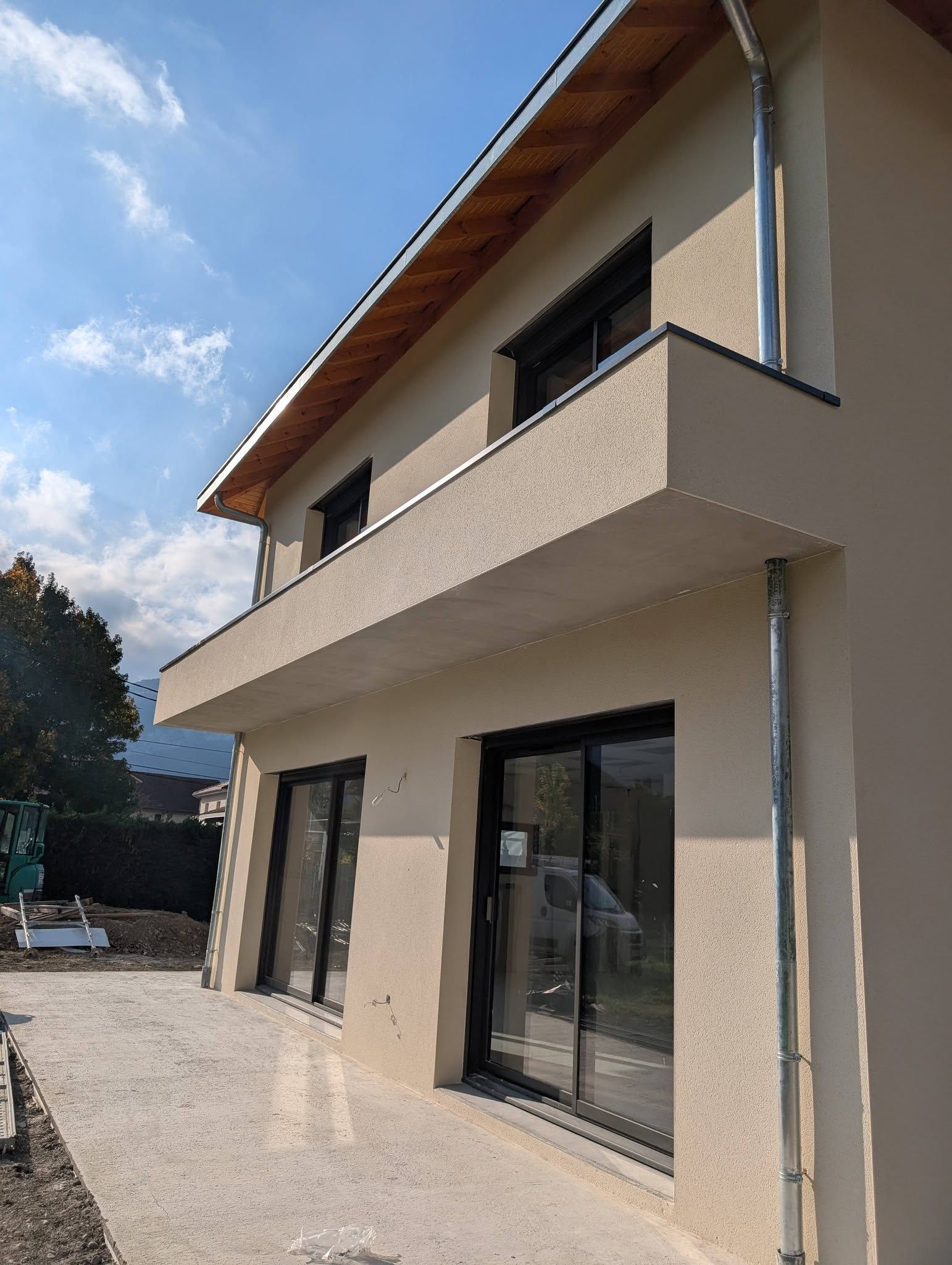 Une maison avec une terrasse et plusieurs éléments de zinguerie : tuyau de descente, couvertine, gouttières.