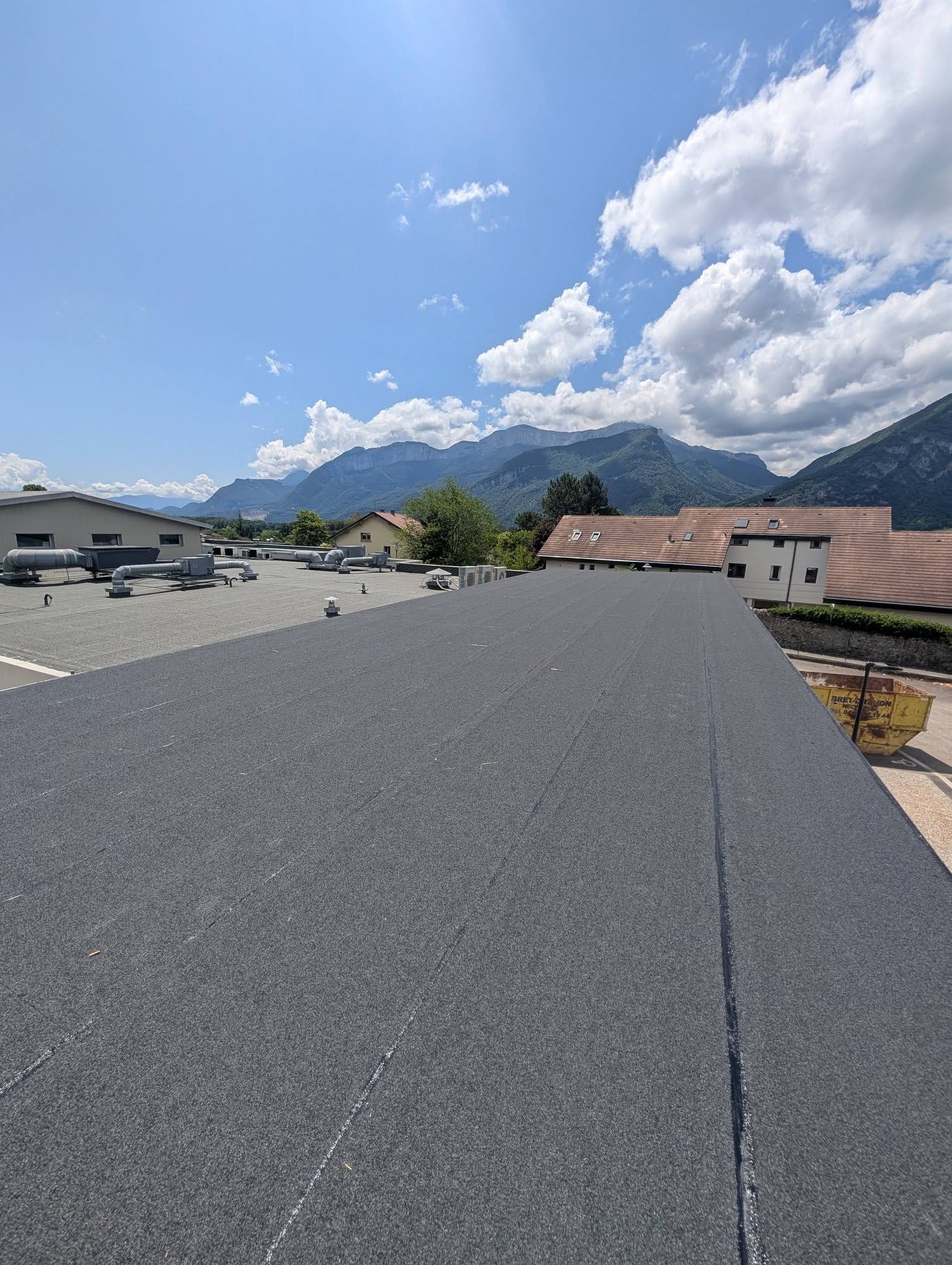 Un toit plat recouvert de bitume chauffé, donnant sur un parking et des montagnes au loin.