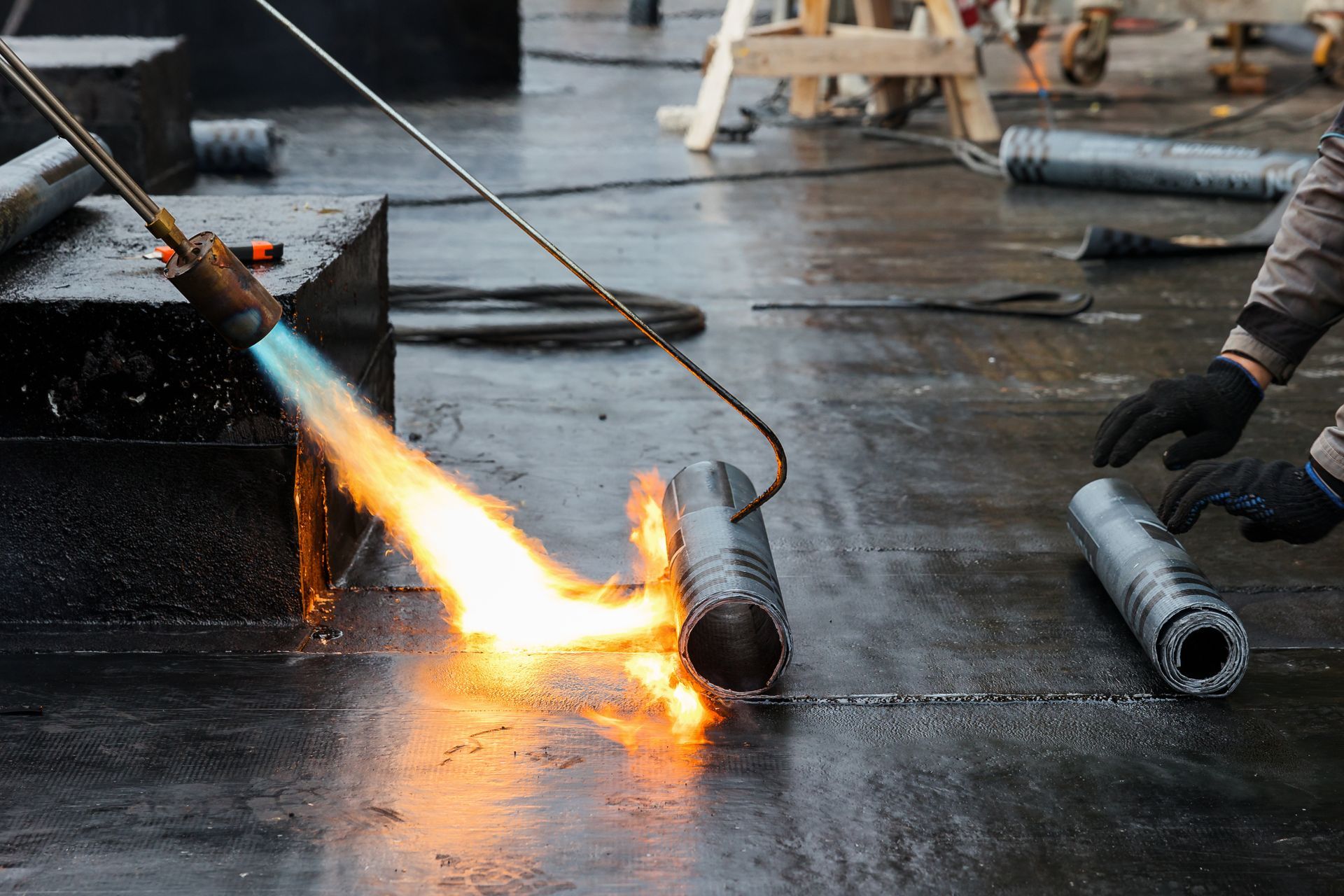 Un artisan applique un rouleau d'étanchéité bitumineuse sur un toit plat.
