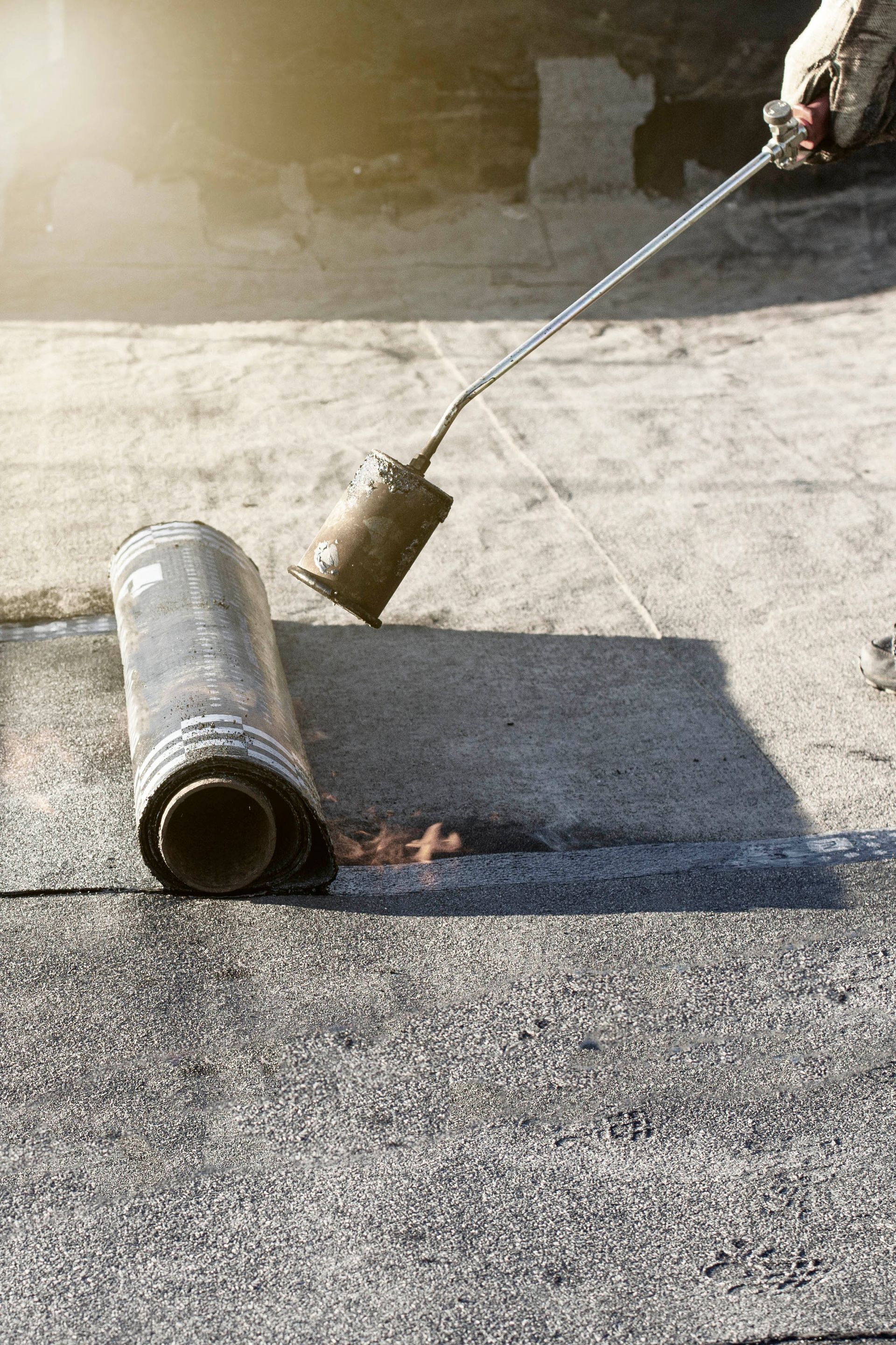 Une personne utilise un chalumeau à propane pour appliquer un rouleau de membrane d'étanchéité bitumineuse sur un toit plat.