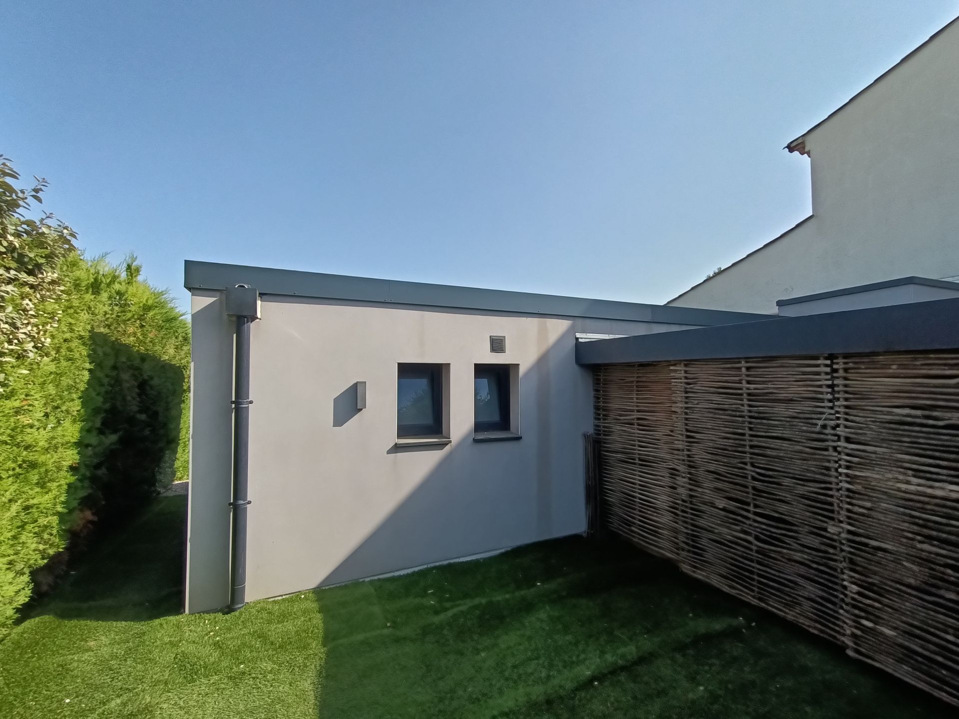 L'extérieur d'un bâtiment au toit plat. Des éléments de zinguerie sont visibles : boîte à eau, tuyau de descente, couvertine.