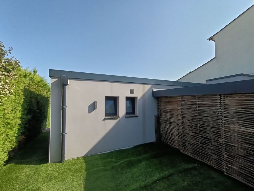 L'extérieur d'un bâtiment au toit plat. Des éléments de zinguerie sont visibles : boîte à eau, tuyau de descente, couvertine.