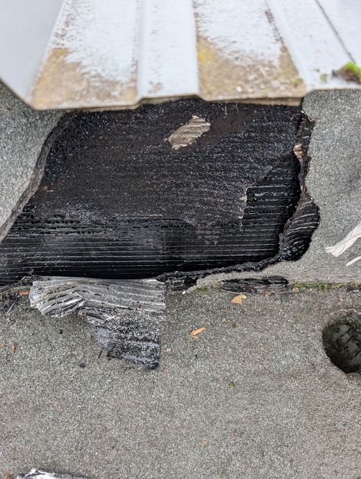 Une zone endommagée d'une toiture-terrasse, laissant apparaître l'isolant noir.