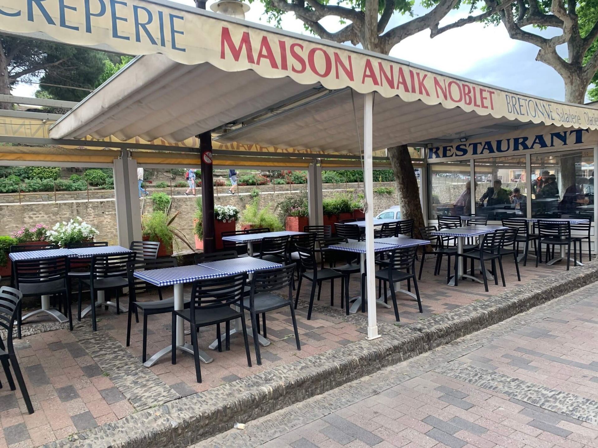 Restaurant en plein air  avec tables, chaises et auvent. Dominée par les tons beiges et bleus.