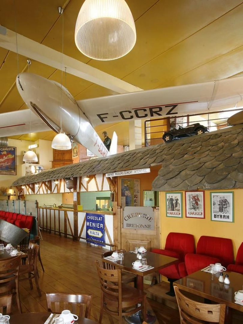 Intérieur du restaurant avec un avion suspendu au plafond et des tables avec des sièges rouges.
