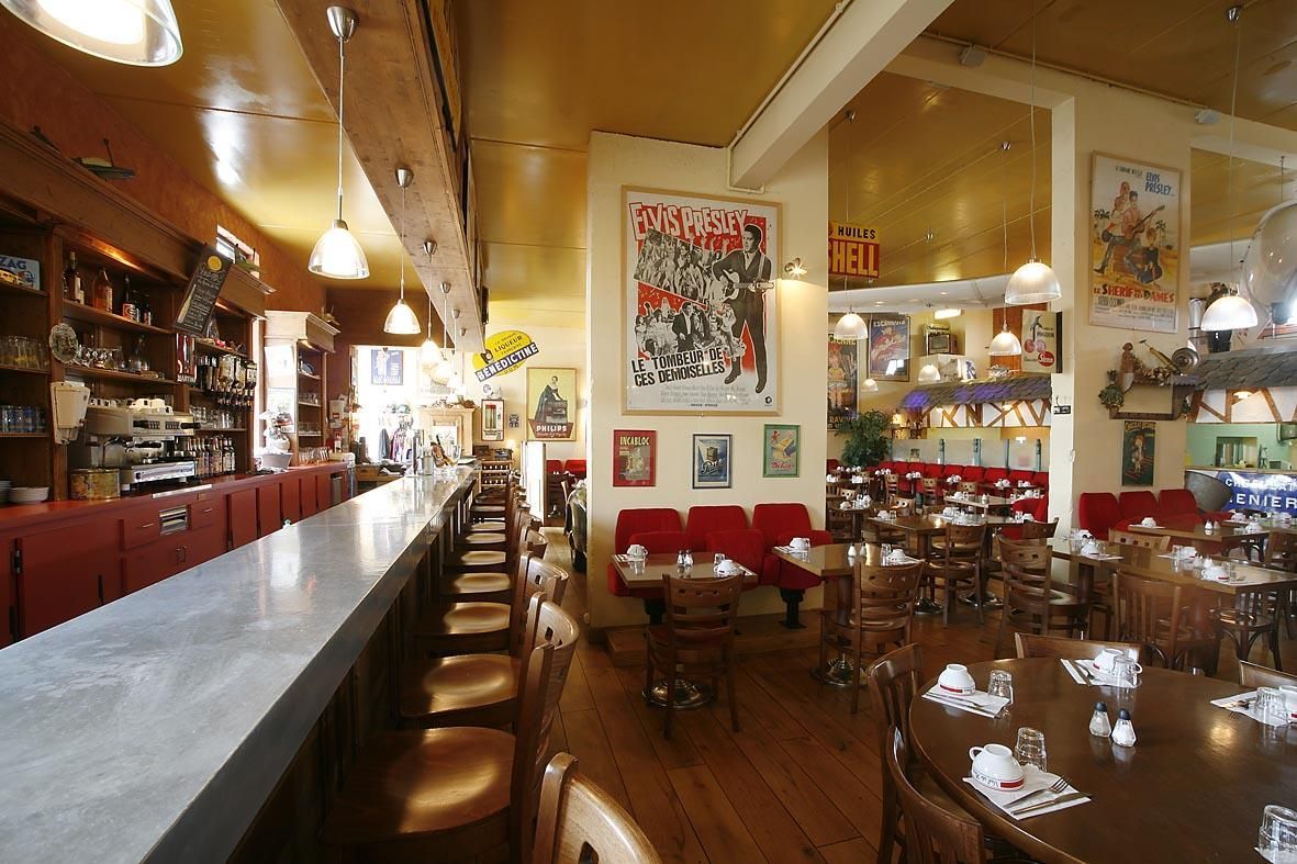 Intérieur d'un restaurant avec un long comptoir, des banquettes rouges et des tables en bois.