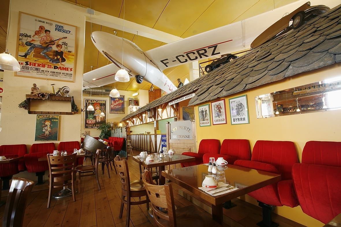 Intérieur du restaurant avec des banquettes rouges, des tables en bois et une maquette d'avion suspendue au plafond.