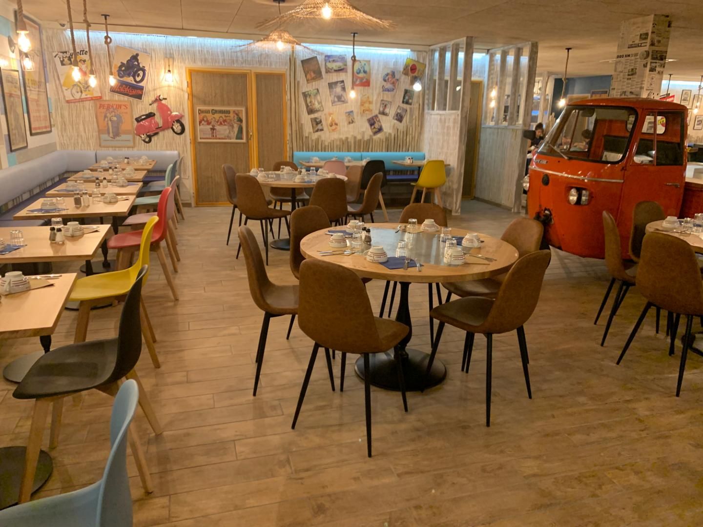 Intérieur de restaurant avec tables et chaises, éléments décoratifs et un camion rouge.