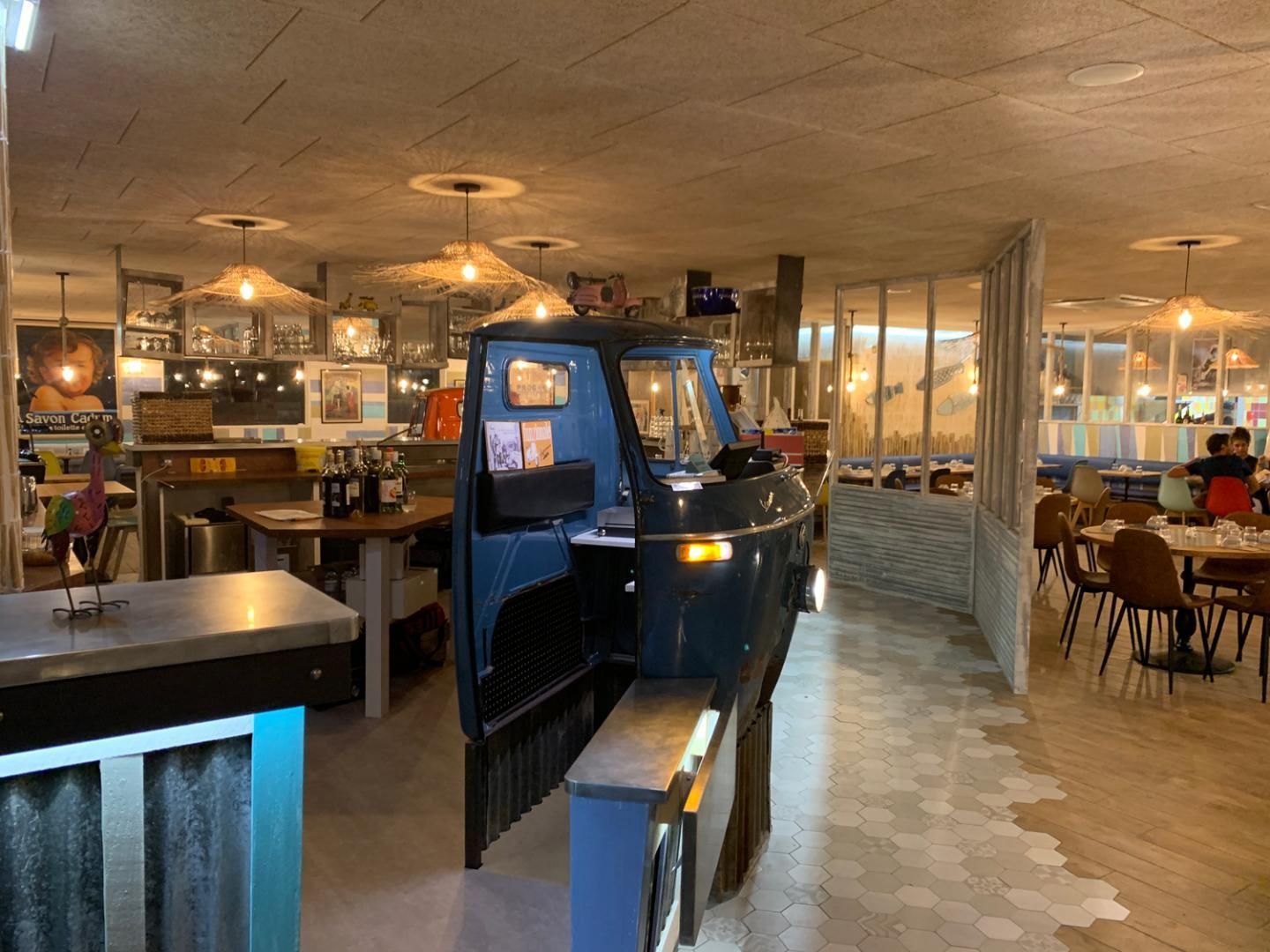 Intérieur du restaurant avec un véhicule bleu foncé comme élément de décoration, tables, chaises et éclairage.