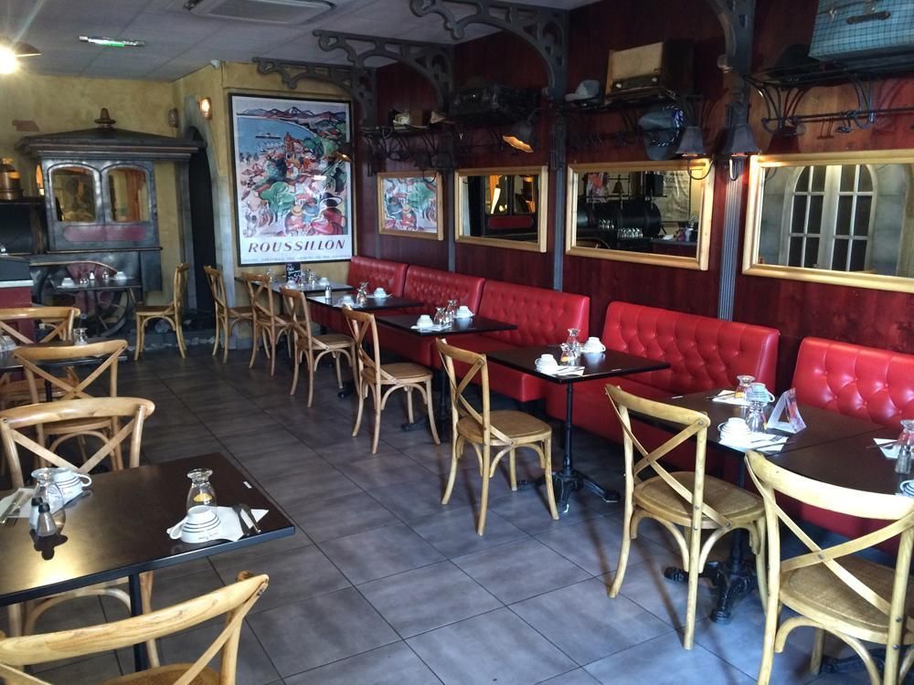 Intérieur du restaurant avec banquettes rouges, tables et chaises en bois, miroirs et affiches décoratifs.