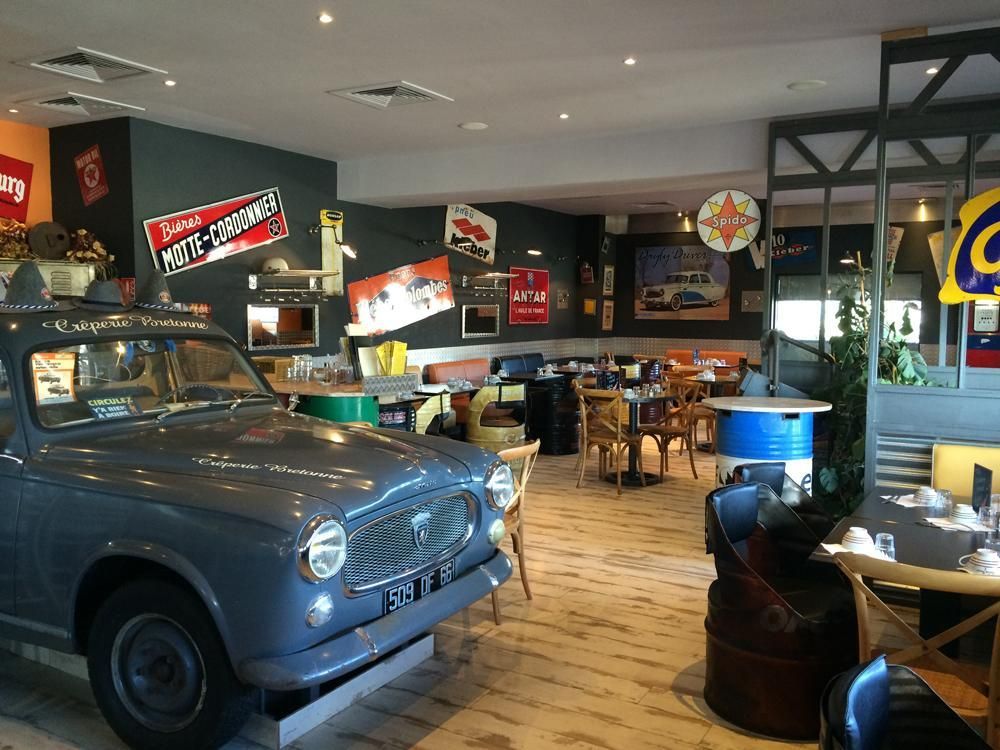Intérieur de restaurant avec une voiture ancienne, des murs ornés d'enseignes et de tables vintage.