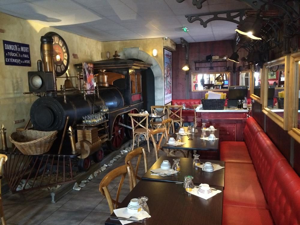 Intérieur du restaurant avec un wagon de train en guise de centre de table, des tables, des chaises et des banquettes rouges.