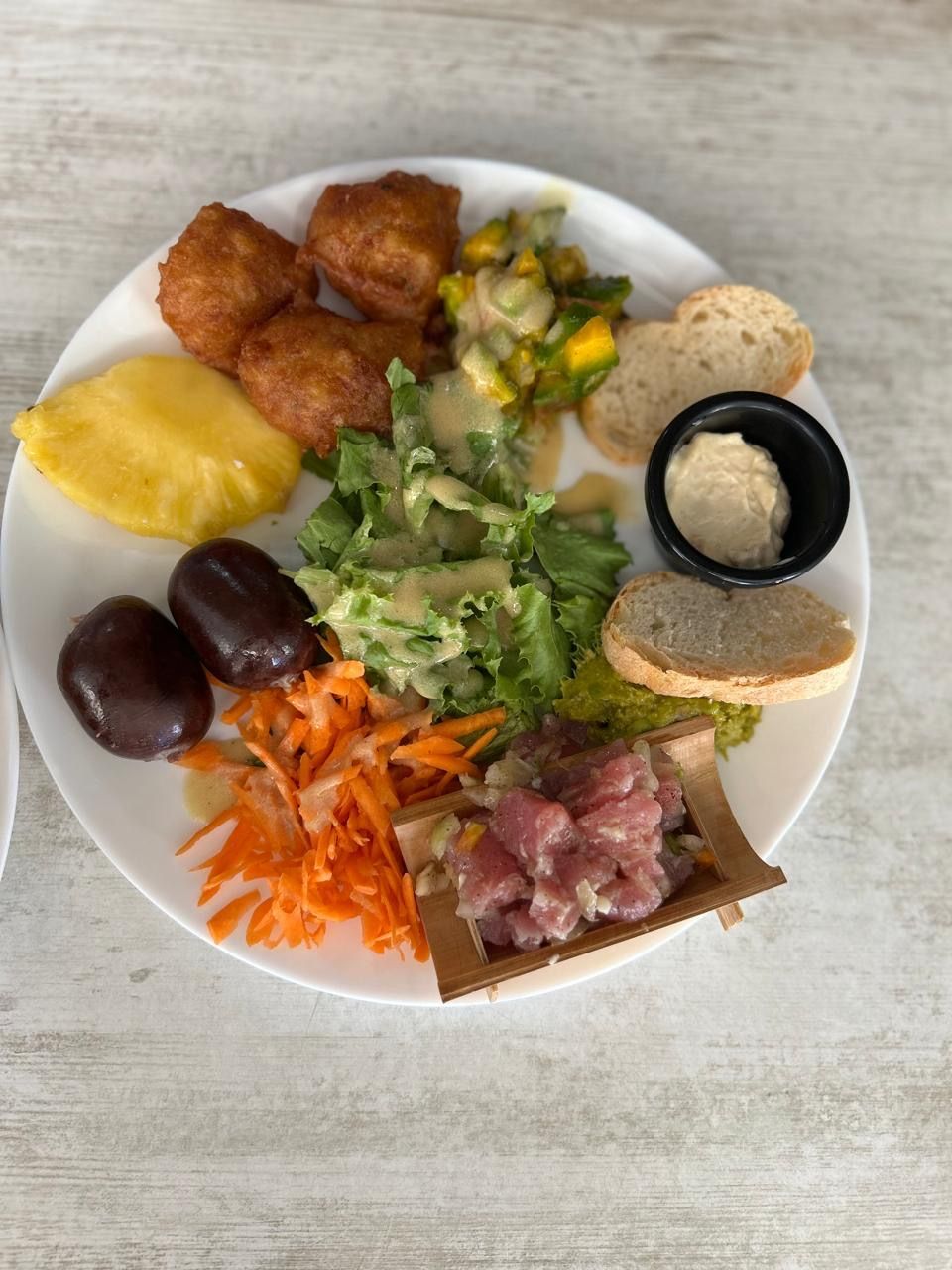 Assiette garnie de mets variés : fritures, salade, dattes, carottes, tartare de thon et pain.