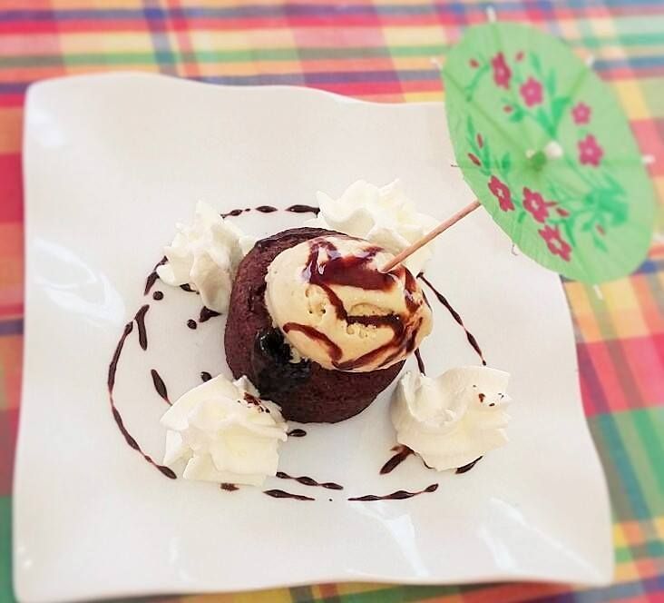 Dessert au chocolat avec glace, crème fouettée et un parasol décoratif sur une assiette blanche.