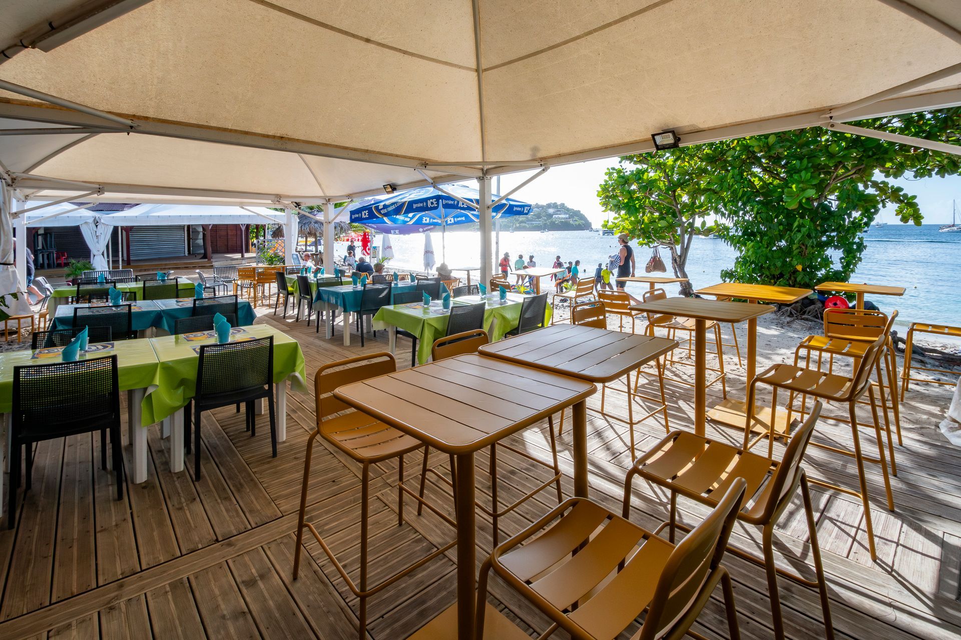 Restaurant en plein air avec tables, chaises et vue sur la plage sous une pergola.