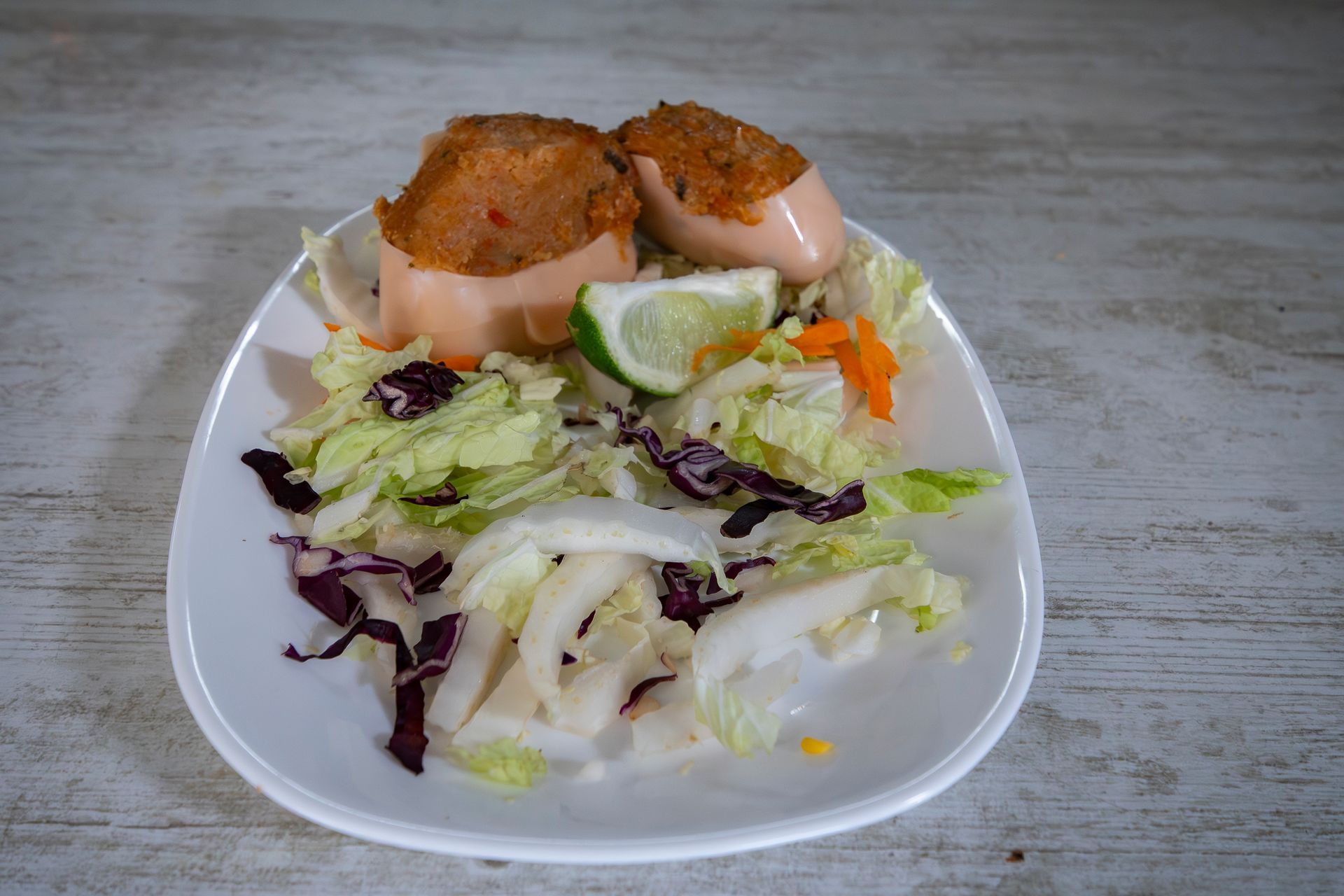 Assiette de saucisses farcies accompagnée d'une salade et d'un quartier de citron vert.