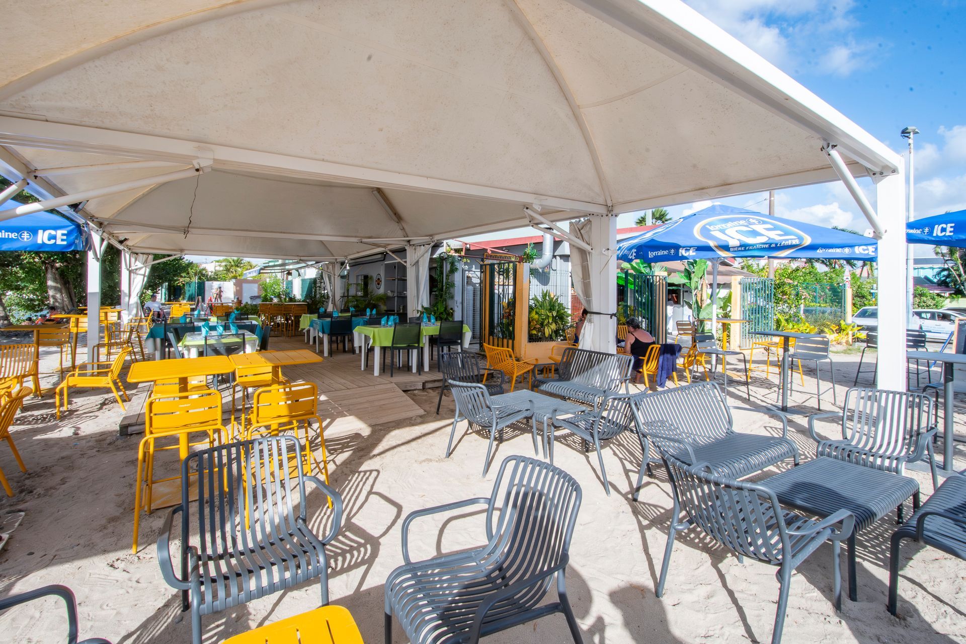 Terrasse de restaurant avec auvent blanc, chaises et tables jaunes et grises.