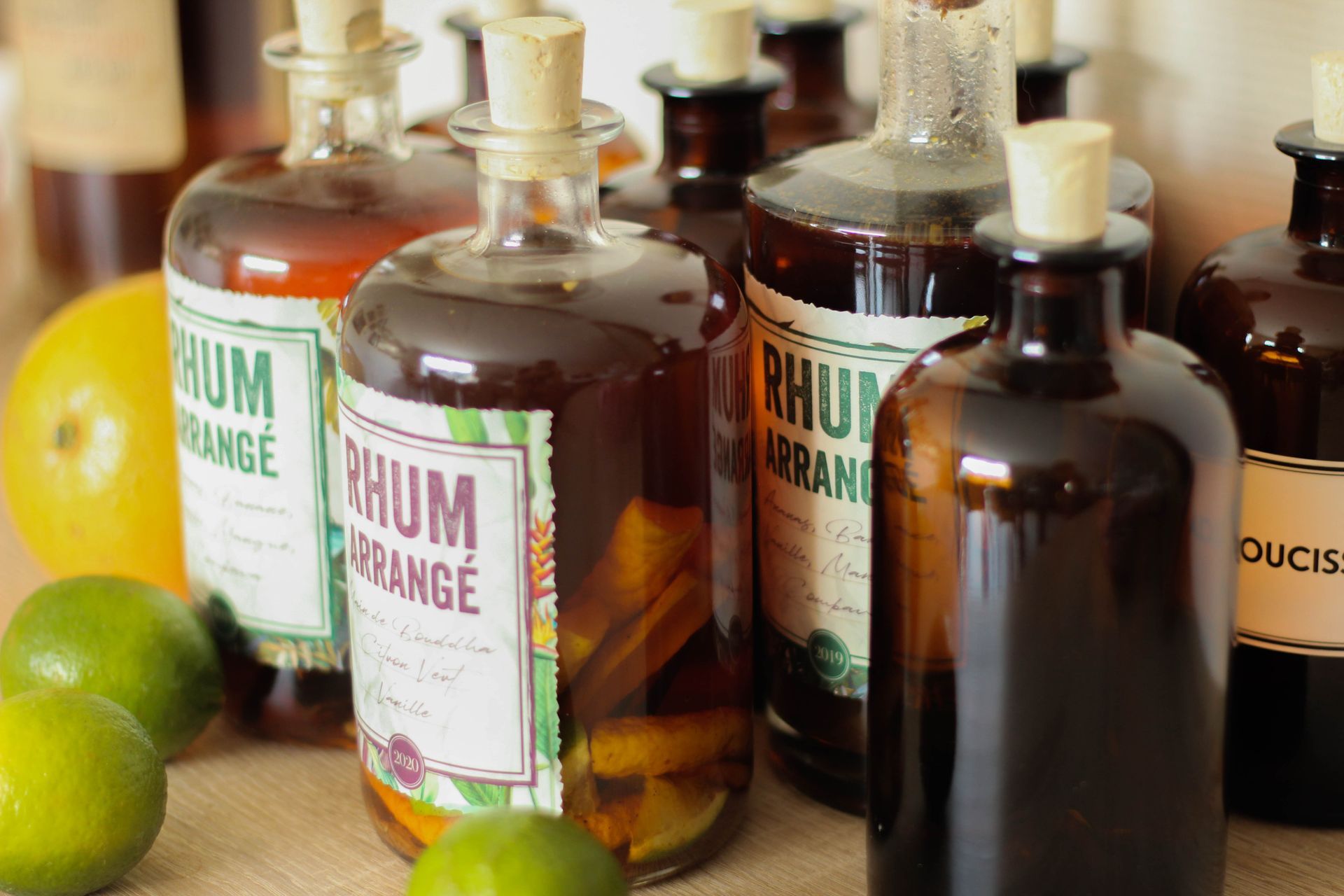 Bouteilles de rhum disposées avec des fruits, devant un citron vert et une orange.