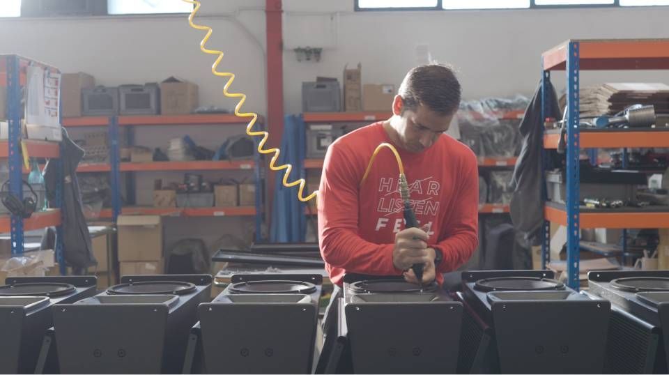 Ein Arbeiter in rotem Hemd und mit Mundschutz montiert Ausrüstung in einer Fabrikhalle.