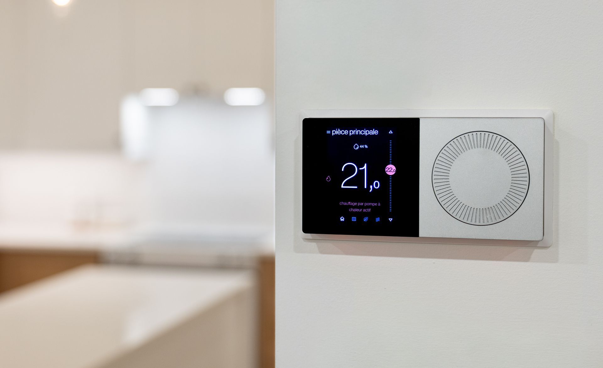 Un thermostat intelligent mural avec un affichage numérique noir indiquant 21,0 degrés, placé dans un intérieur de maison flou.
