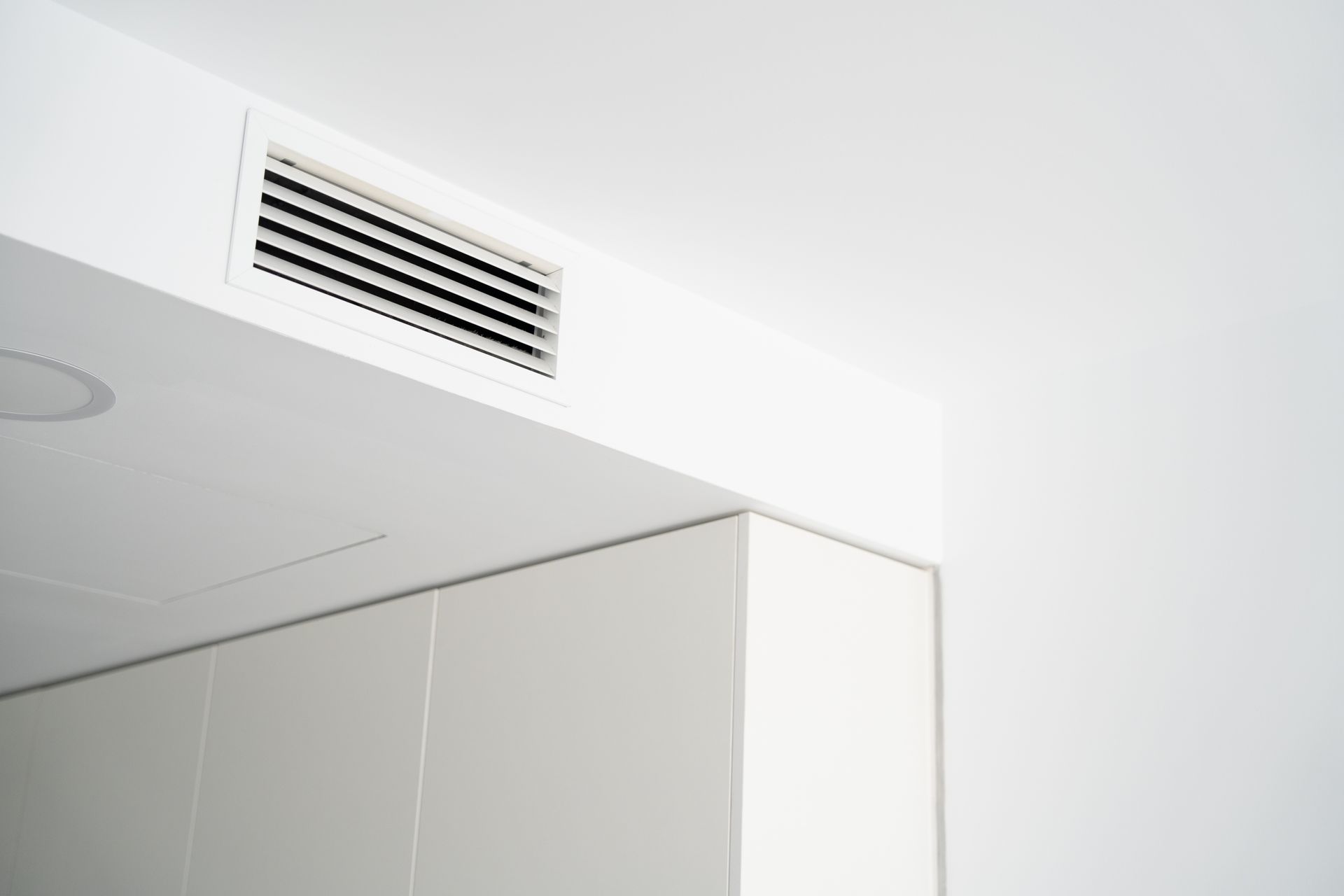 Une grille d'aération rectangulaire blanche fixée au plafond blanc au-dessus d'une armoire murale.